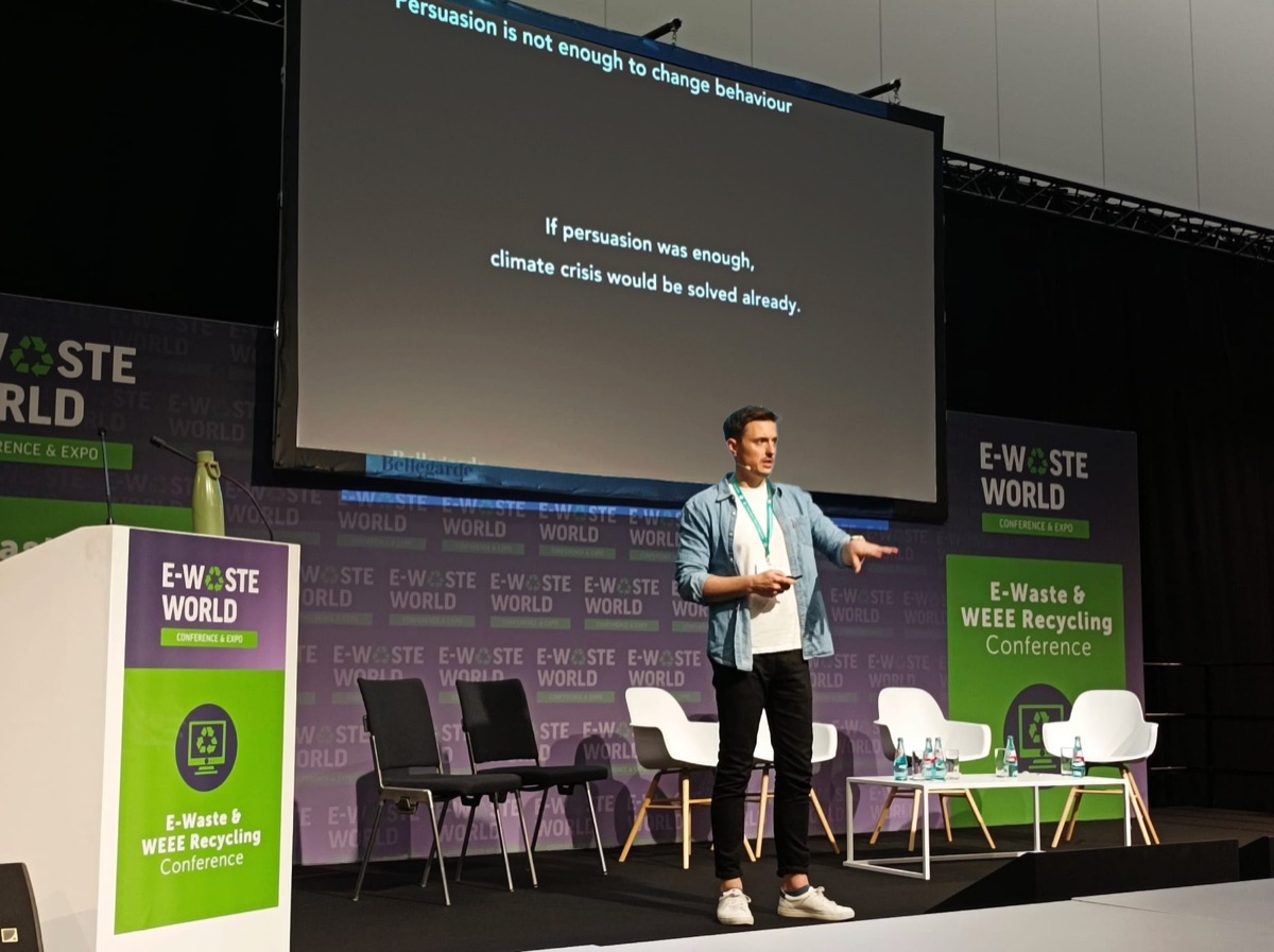 Dimitri Naczaj speaking on stage, next to a slide that reads: if persuasion was enough, climate crisis would be solved already.